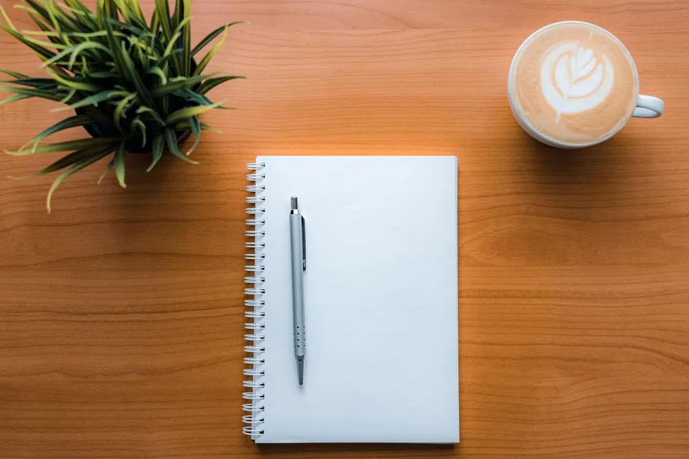 Notebook, pen, plant and coffee on a wooden desk
