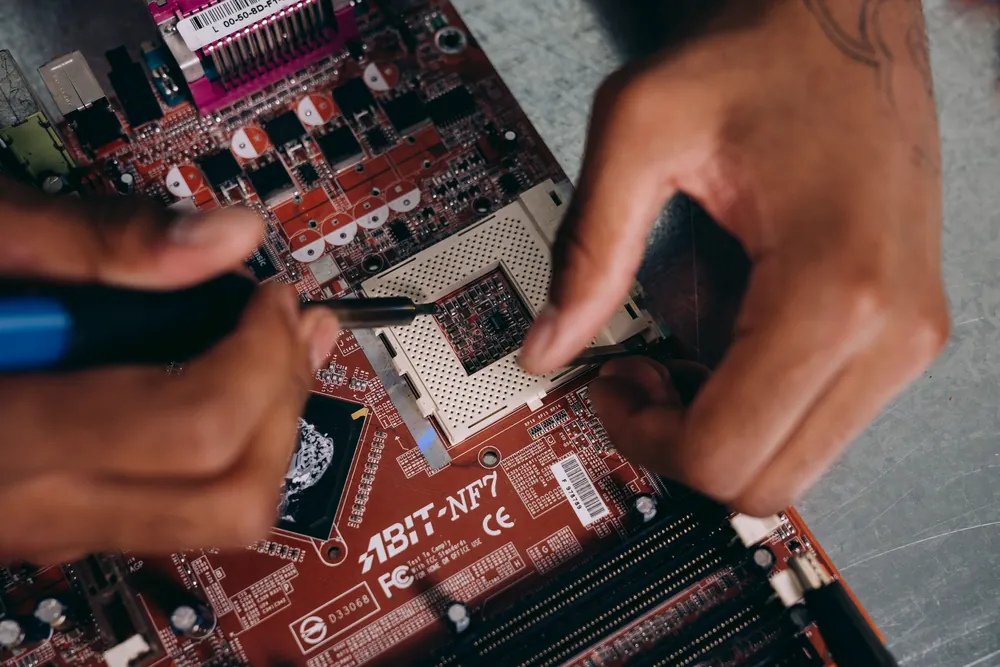 Hands repairing a computer motherboard with a screwdriver